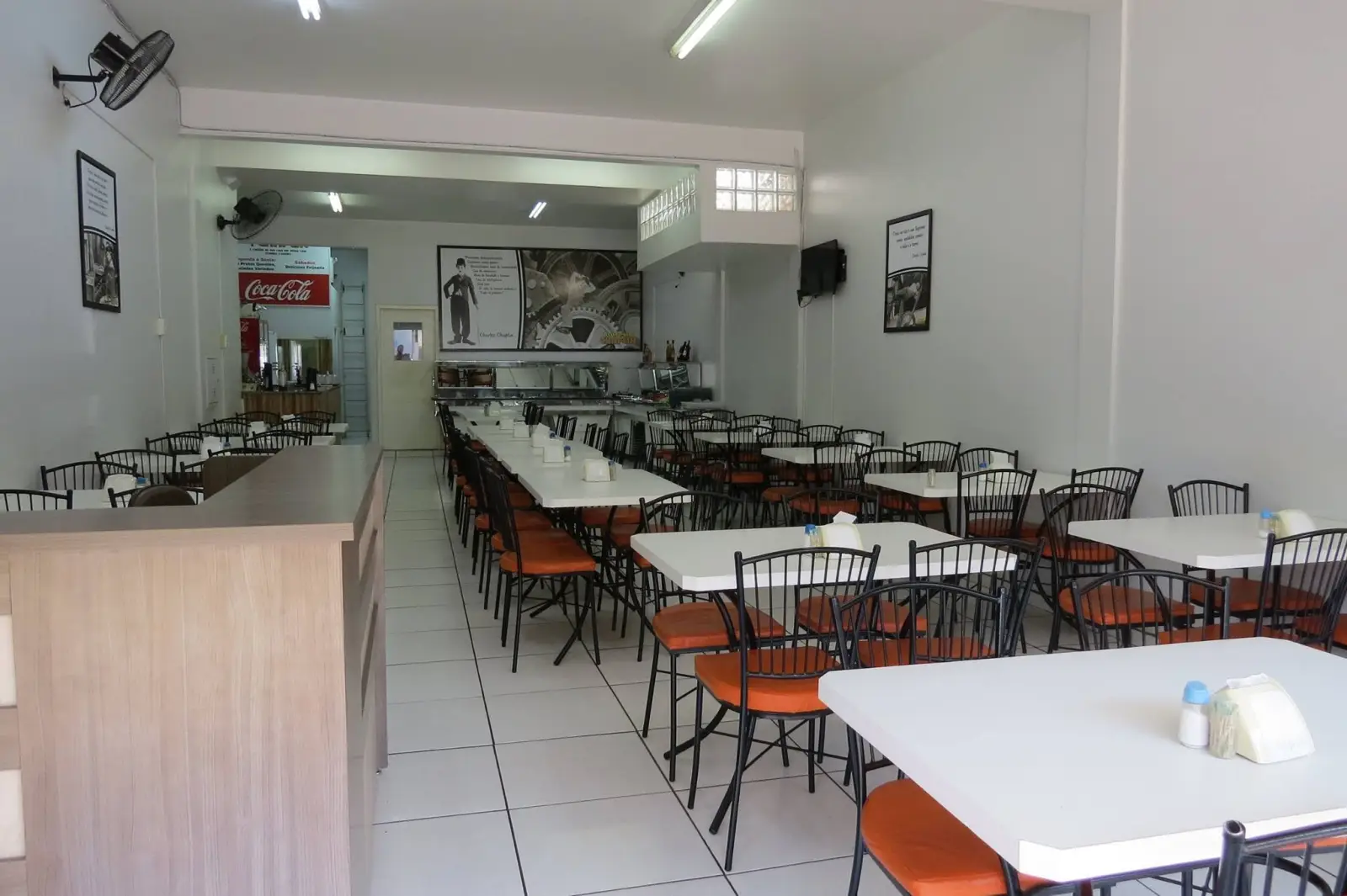 Salão do restaurante com mesas brancas e cadeiras laranja